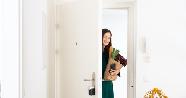 Frau mit Einkäufen öffnet die Haustür, die mit dem elektronischen Türschloss von Nuki gesichert ist
